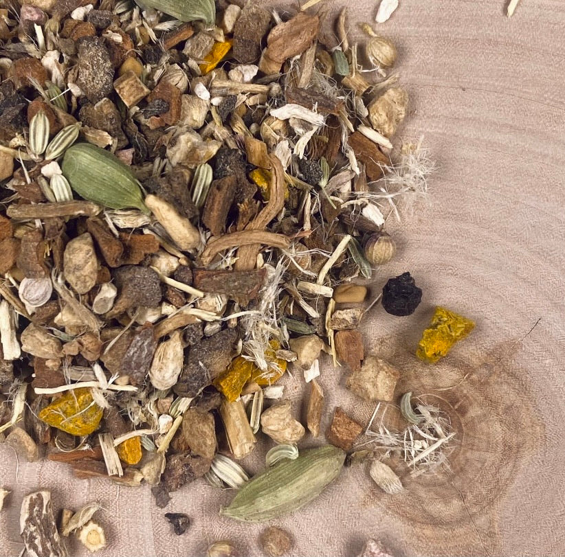 Splash of Root Detox Tisane on birch wood, showcasing cardamom pod, dandelion root and turmeric .