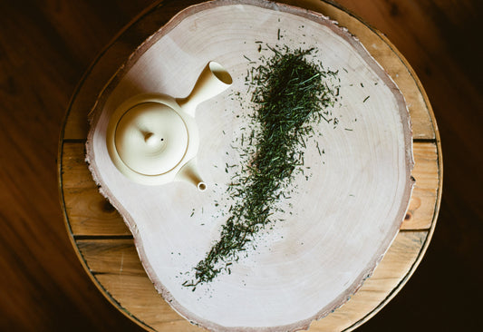 View from above of a tea pot and an alluring dash of organic Sencha tea on bich cut slice, sitting on a coffee Table.