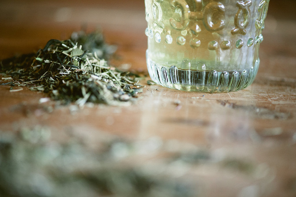 Cup of infused orange blossom green tree with the loose leaf blend beside it on a faded counter.