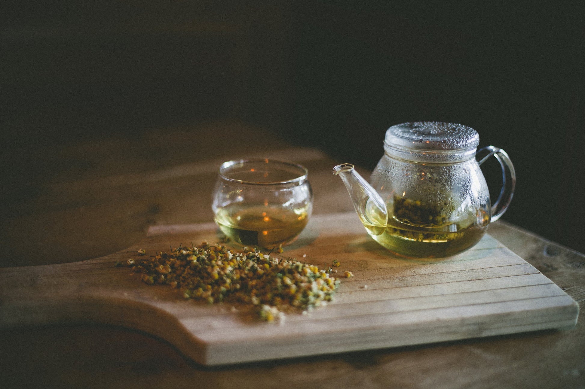 Tea pot infuseing Chamomile Blossoms in a winderful evening setting on a wooden table.