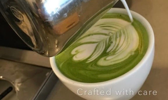 Person making a perfect cup of matcha latte and shocasing her beautiful art of a flower made with milk.
